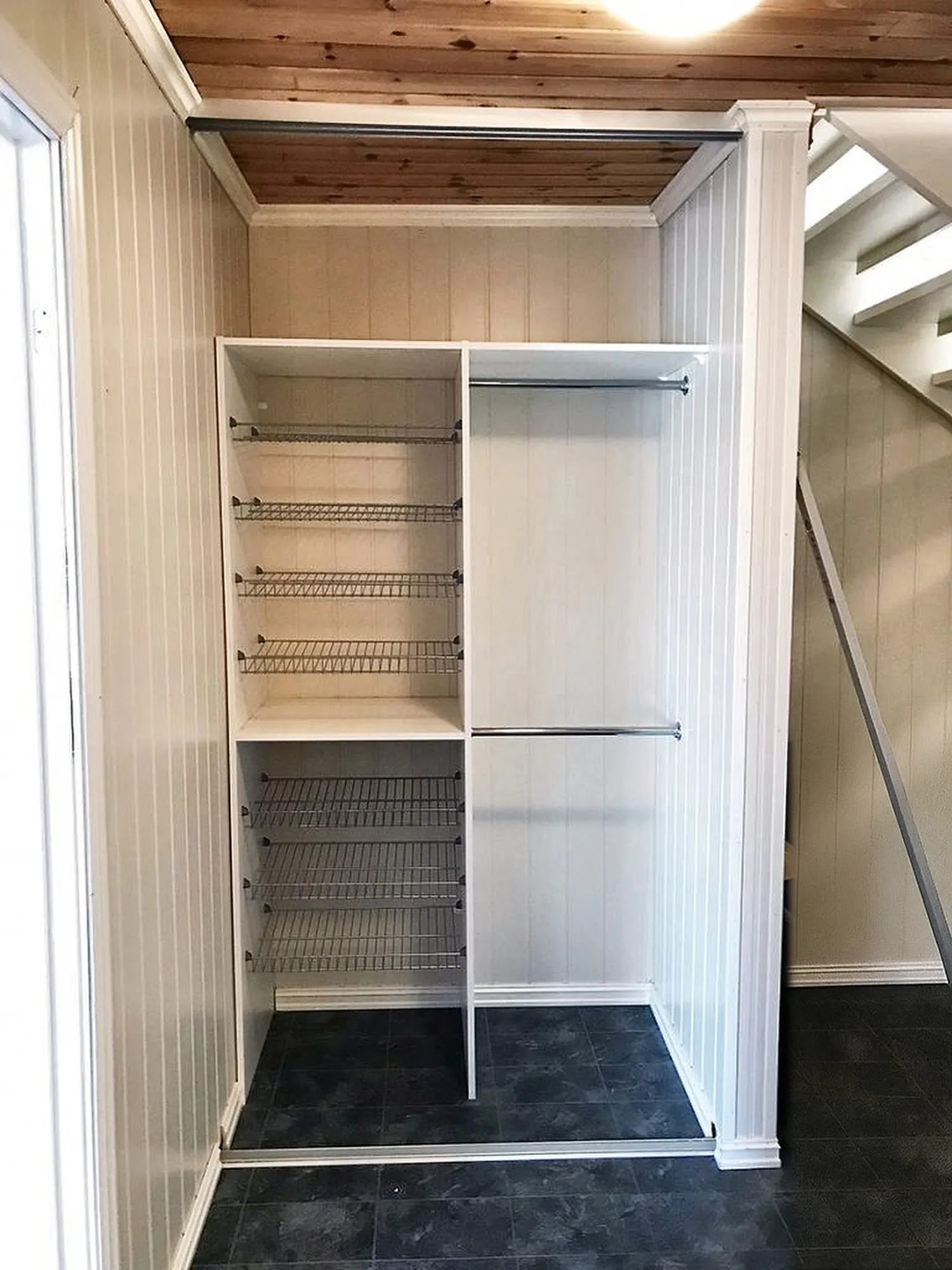 Entrégarderobe mot hvit panelvegg med hyller, hengestang og trådkurver