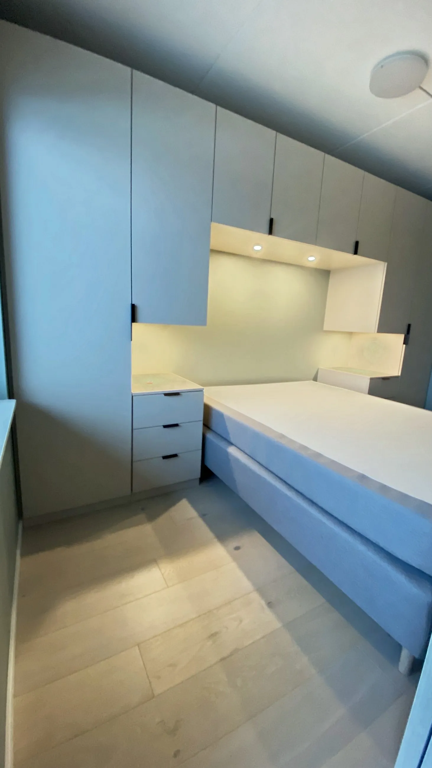 Blågrå skapvegg rundt sengen, med opplyst nisje bak sengegavlen