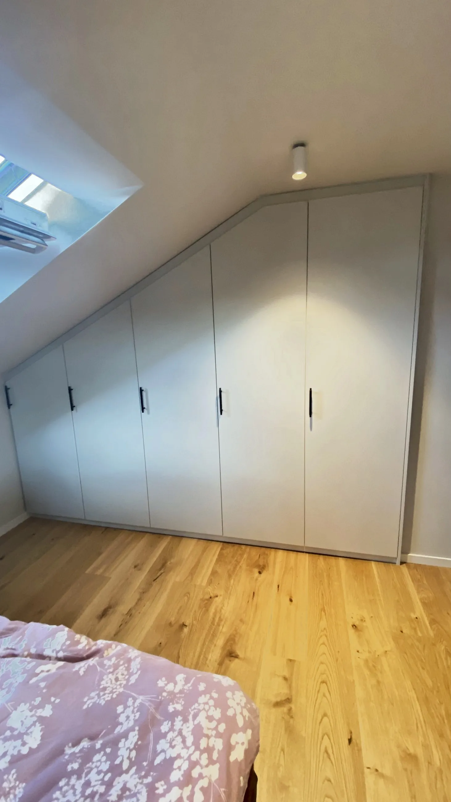 Hvit skråtaksgarderobe med hengslede dører langs kneveggen, under takvinduet