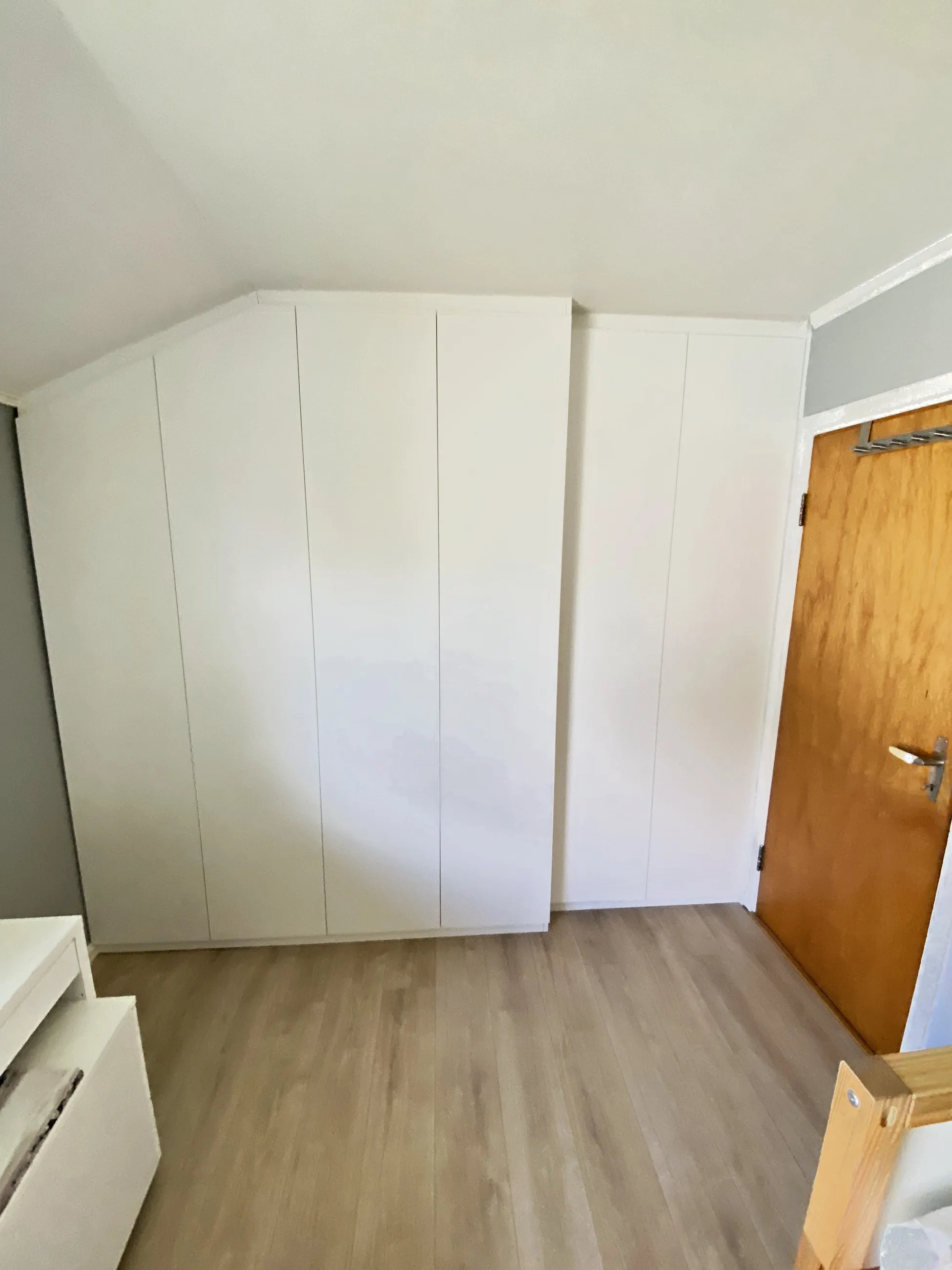 Hvit skråtaksgarderobe med glatte fronter, tilpasset skråtaket på loftsrommet