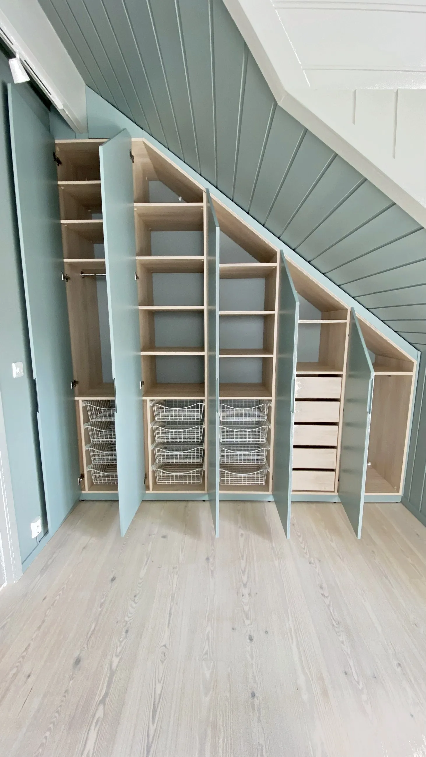 Skråtaksgarderobe i mintgrønt med åpne dører, trådkurver, hyller og skuffer