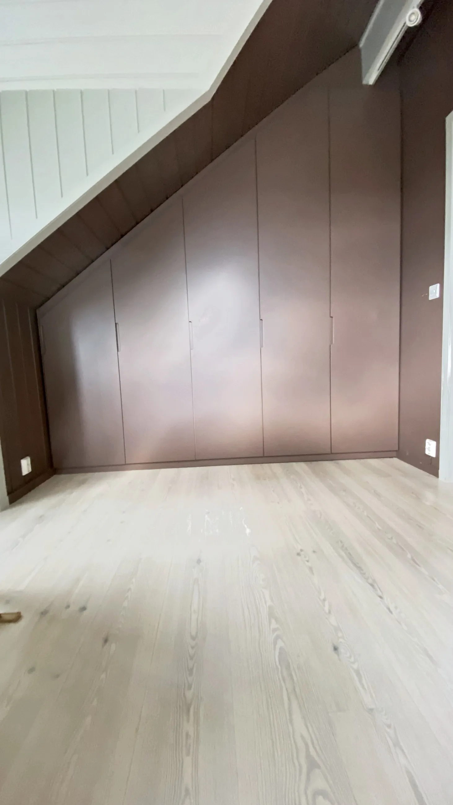 Mørkebrun skråtaksgarderobe som følger takvinkelen fra gulv til møne