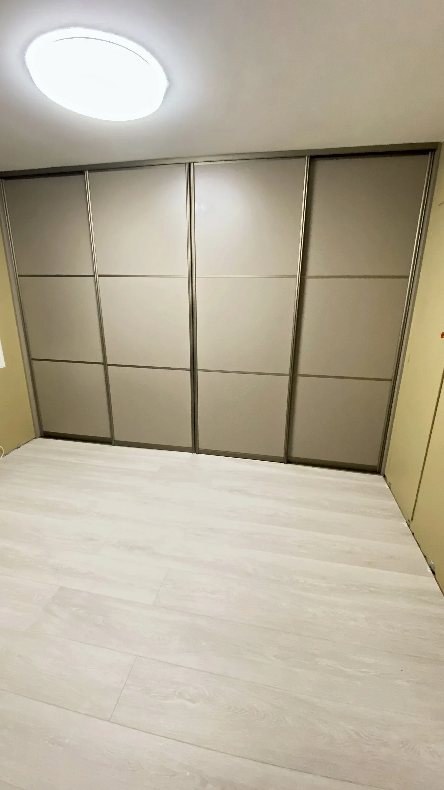 Skyvedørsgarderobe i beige glass med smale sprosser, montert vegg til vegg