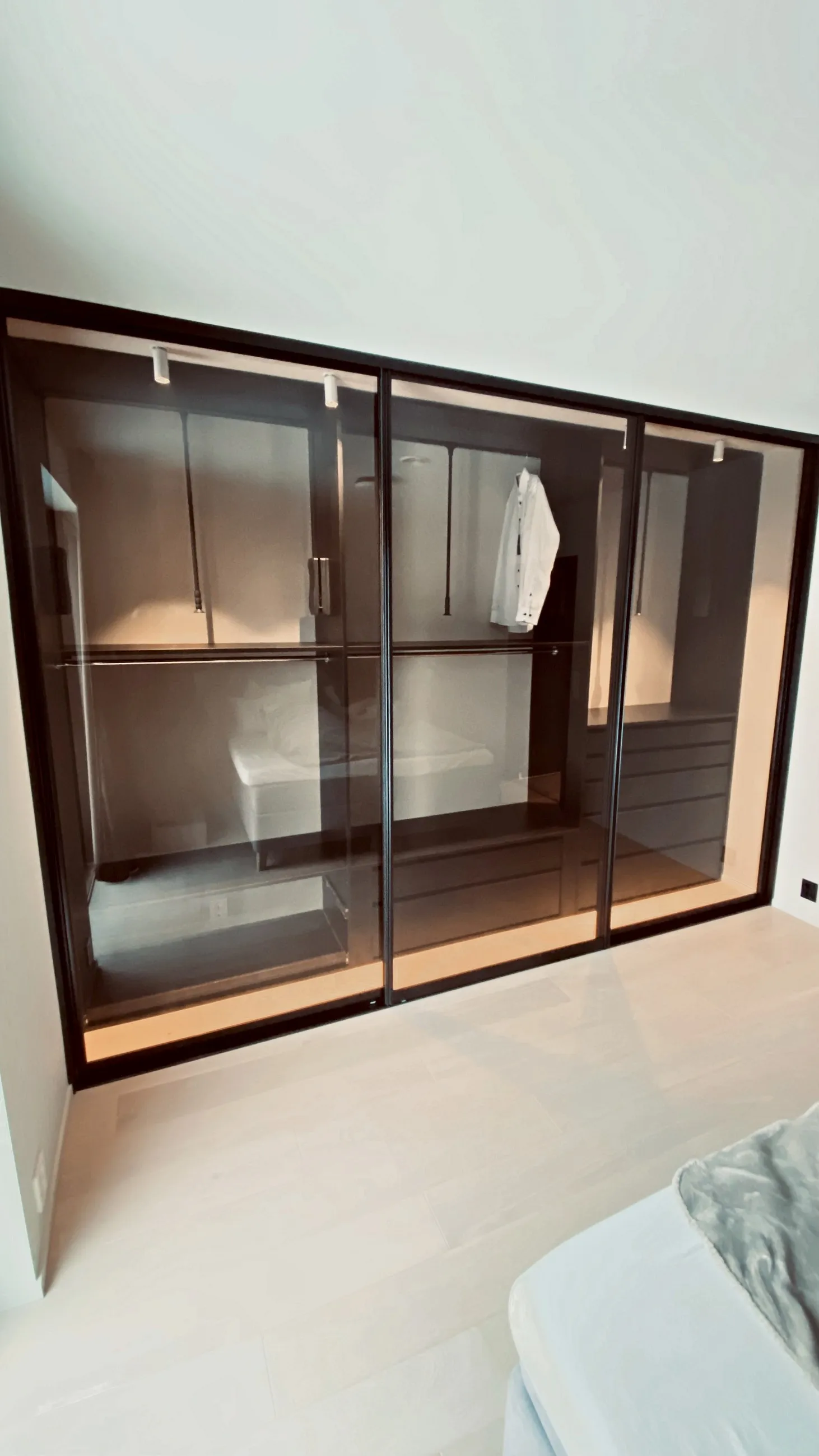 Garderobe med gjennomsiktige glassdører i bronsefarget ramme, med hyller og hengestang synlig