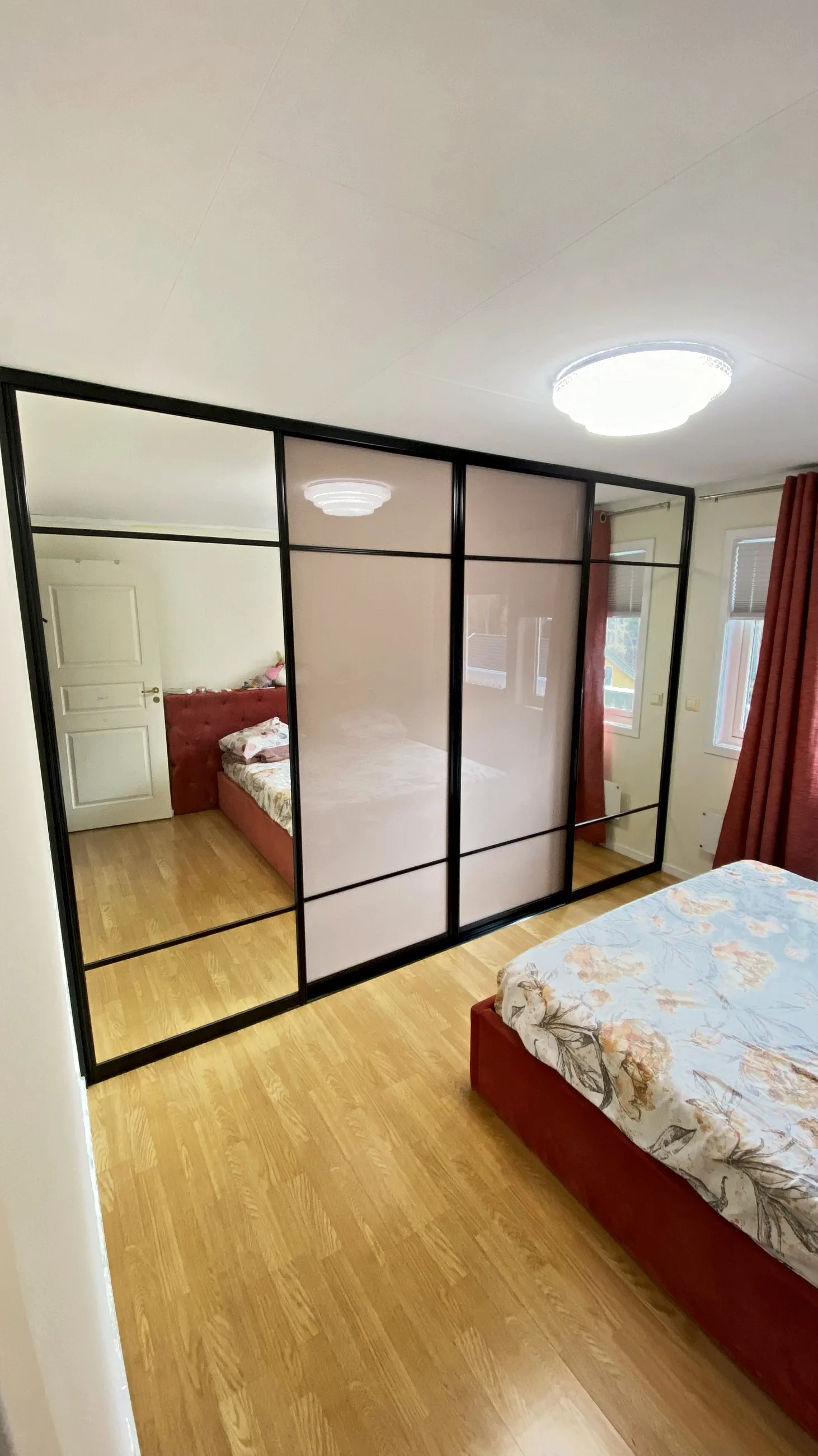 Skyvedører med speil og støvrosa glassfelt i svart ramme på et soverom